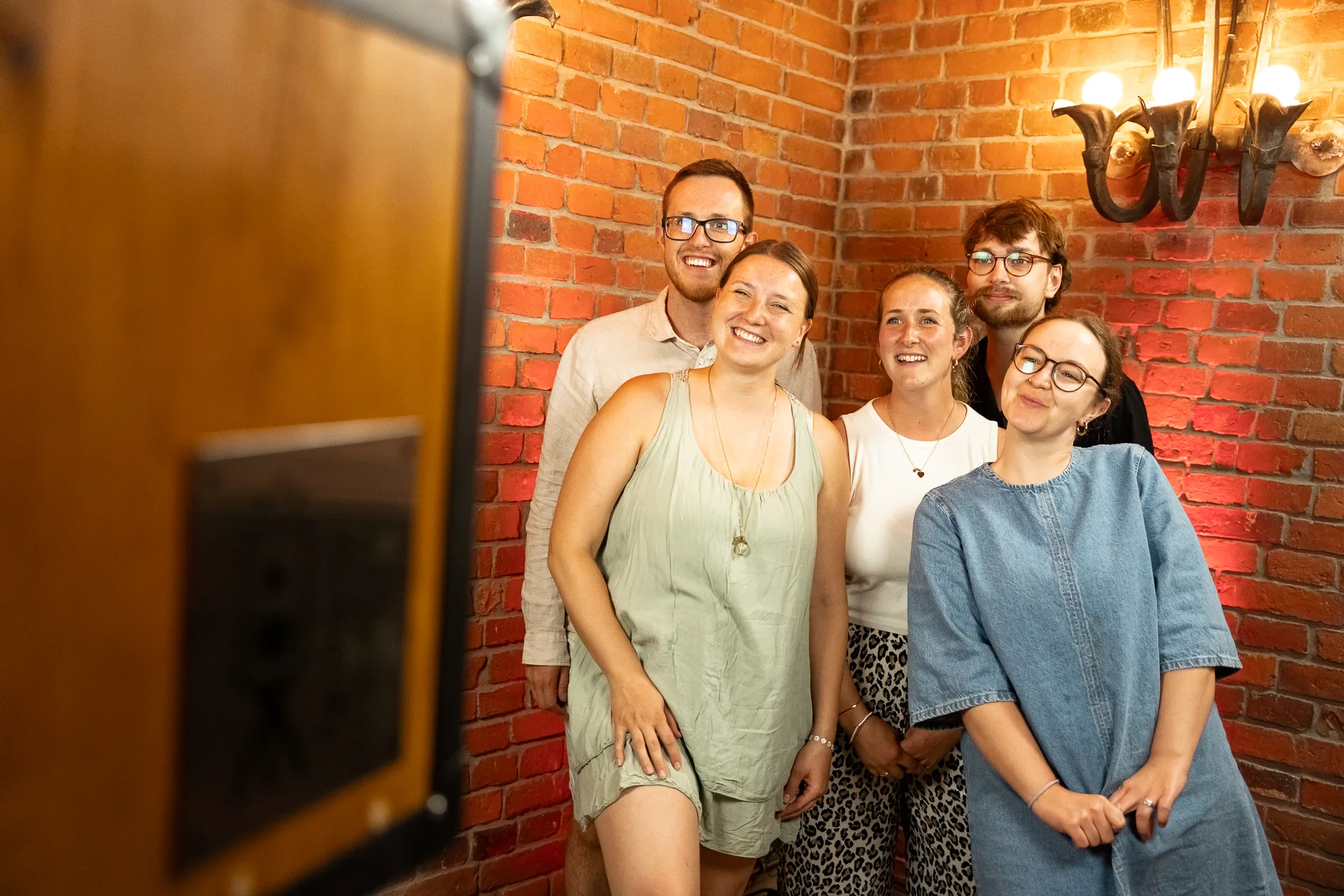 Gäste stehen vor der fernbild.fotobox vor einer Backsteinwand und schauen lachend in die Kamera